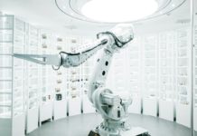 Vratky Zalanda v Německu a Polsku třídí roboti s umělou inteligencí Bílé průmyslové robotické rameno mezi regály s očíslovanými skladovacími boxy